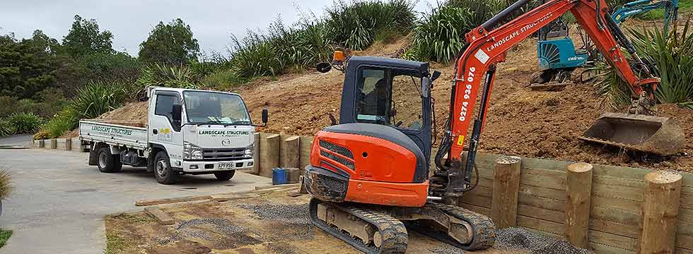 Earthmoving contractor spreading topsoil after constructing new retaining wall in east Auckland